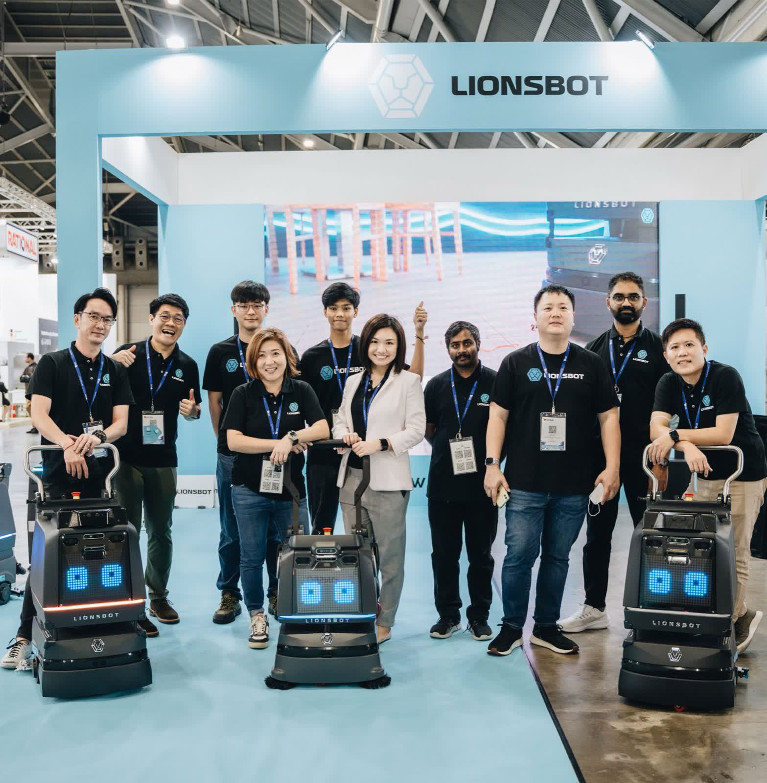 The LionsBot team on their stand at FHA-HoReCa Singapore 2022, with three compact R3 cleaning robots lined up in front of them