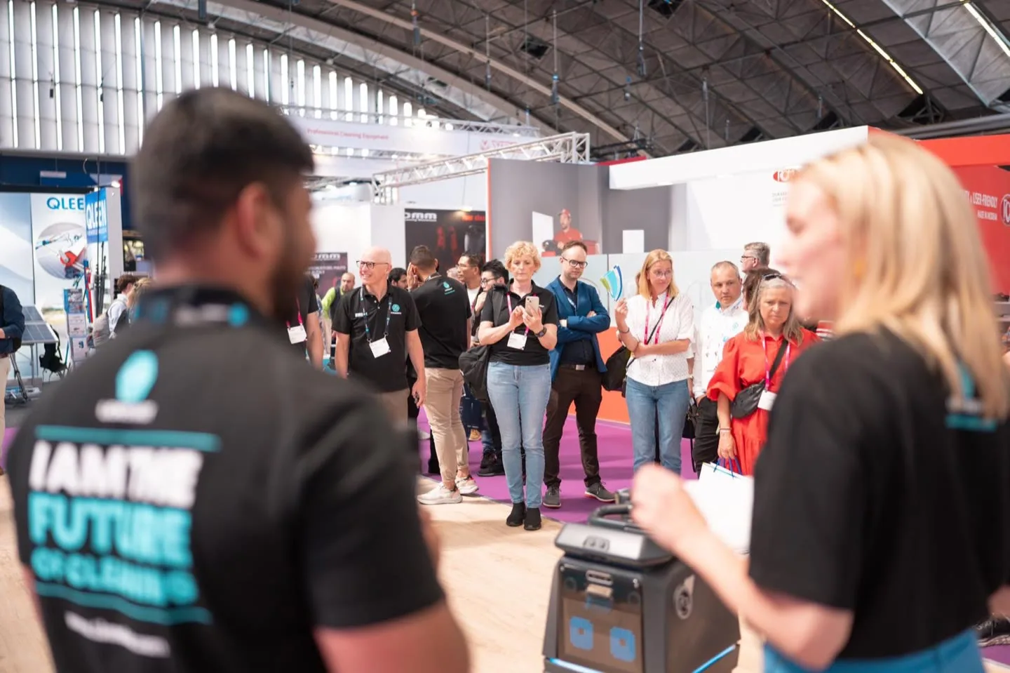 Visitors gathered in a semicircle watching a live demonstration of a LionsBot cleaning robot, with two LionsBot staff in the foreground