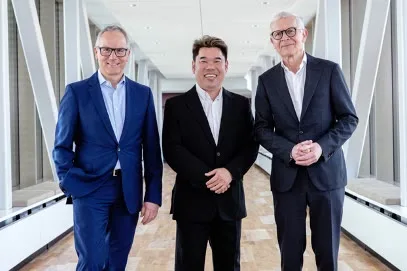 Three executives standing together in a bright office corridor: Nilfisk CEO Rene Svendsen-Tune, LionsBot CEO Dylan Ng and Nilfisk CFO Reinhard Mayer