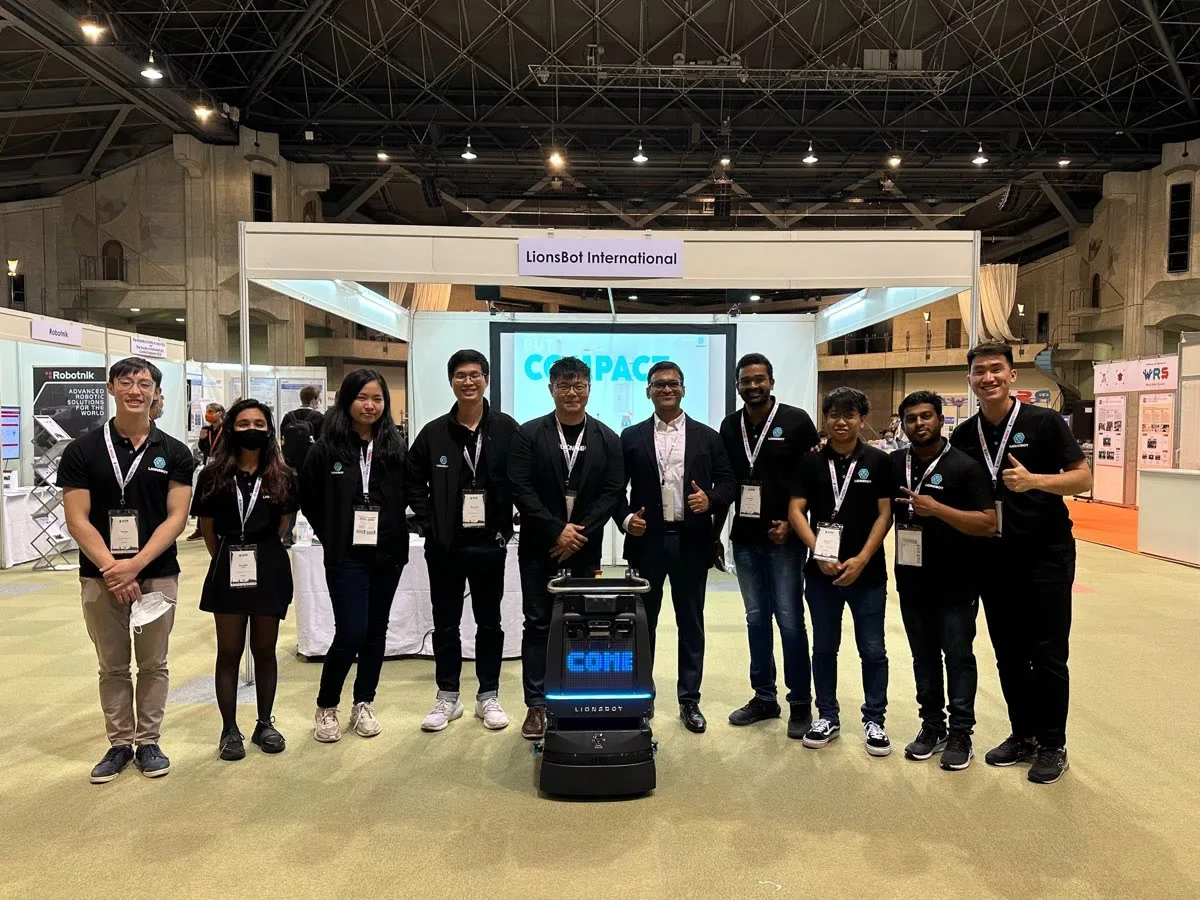 Members of the LionsBot team at their stand in Kyoto, with an R3 Scrub cleaning robot in front of them