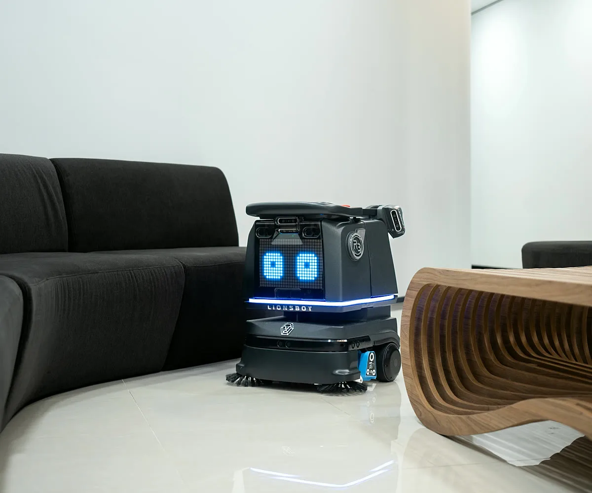 A LionsBot R3 Vac vacuuming the floor between a sofa and a low table in a lounge