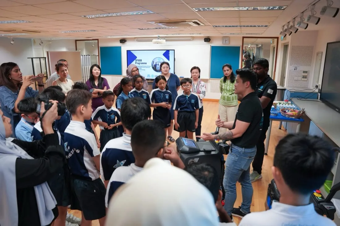 Schoolchildren gathered around a LionsBot engineer demonstrating a robot at a SPARK Programme session
