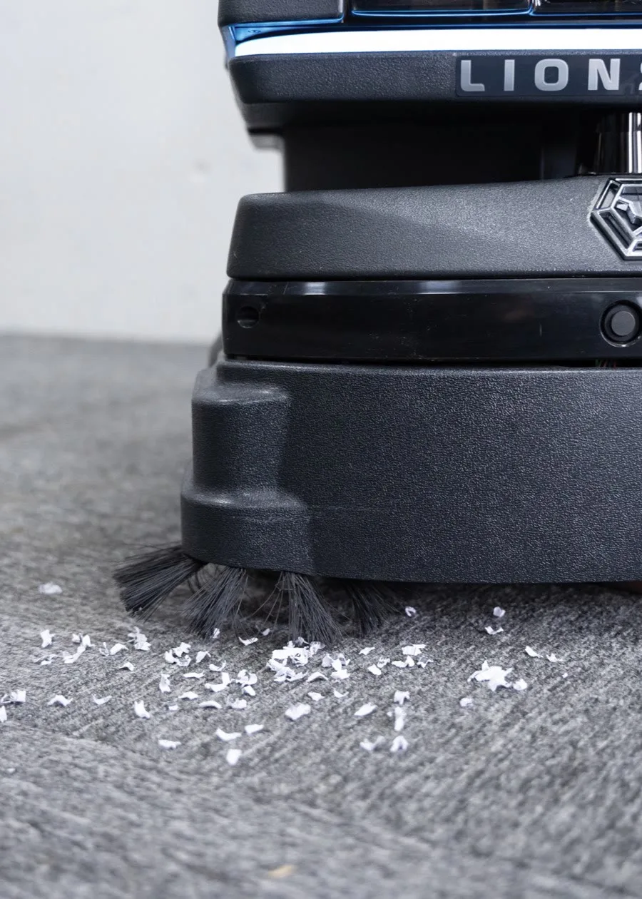 A close view of the LionsBot R3 Vac lifting scattered debris from a carpeted floor
