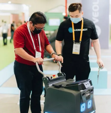A visitor trying the handle controls of a LionsBot robot with a team member at the CleanEnviro Summit