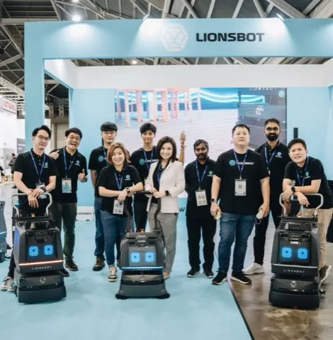 The LionsBot team standing with three robots at their FHA-HoReCa exhibition stand in Singapore
