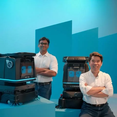 The R3 Vac and R3 Scrub Pro presented with two members of the LionsBot team against a blue studio backdrop
