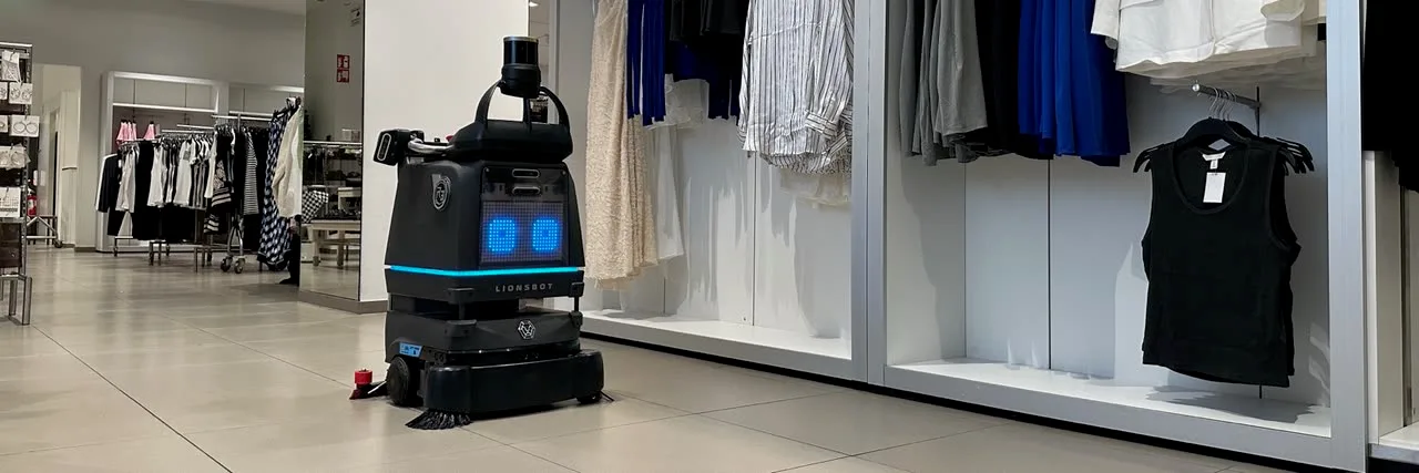 A LionsBot R3 Scrub Pro scrubbing the floor of a retail store aisle beside clothing displays