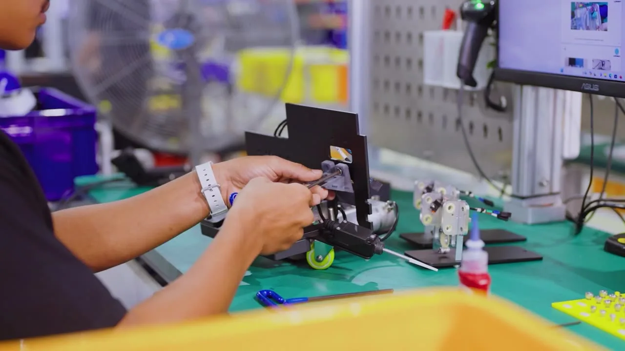 A LionsBot engineer assembling a robot component at a workbench, with test equipment and parts trays around them