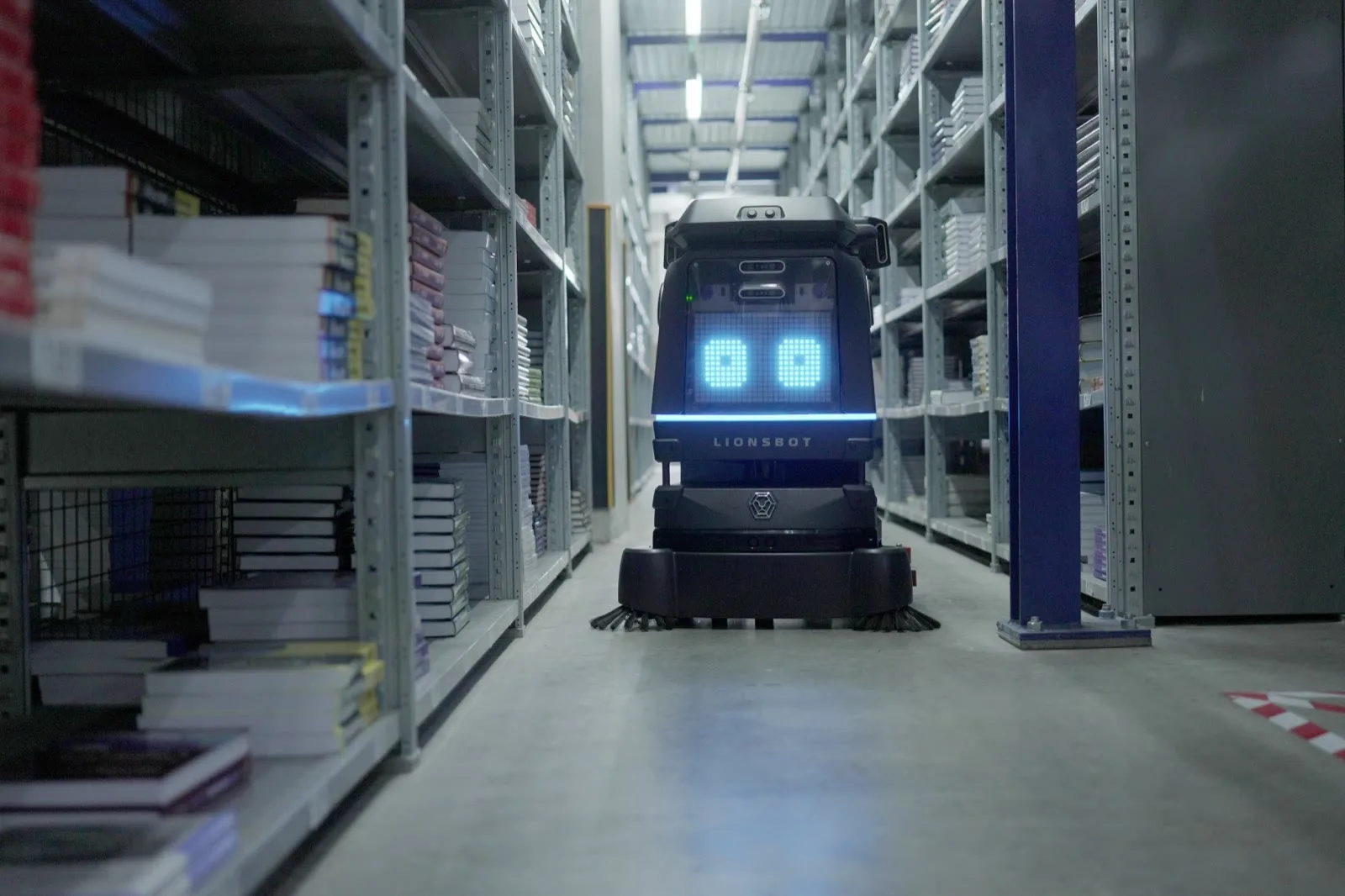 A LionsBot R3 Scrub Pro cleaning a concrete aisle between tall metal racks stacked with books